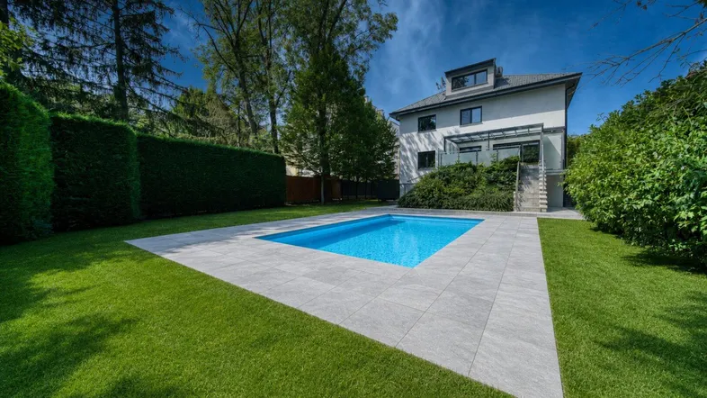 Moderner Gartenbereich mit Swimmingpool, gepflegtem Rasen und Hecken um das Haus.
