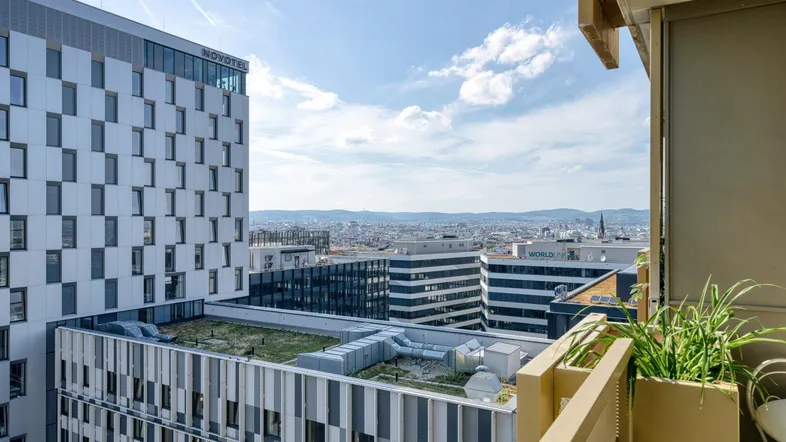 Panoramablick von einem Balkon auf die Stadtlandschaft mit modernen Gebäuden und fernen Bergen.