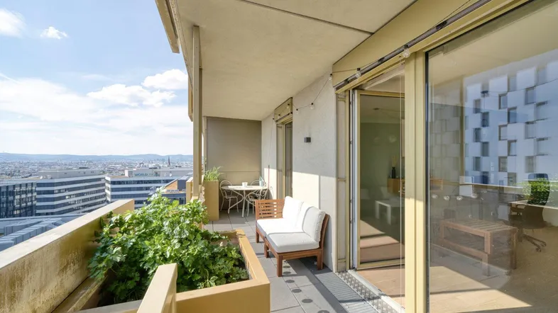 Geräumiger Balkon mit Sitzgelegenheiten, Pflanzen und weitem Stadtblick unter blauem Himmel.