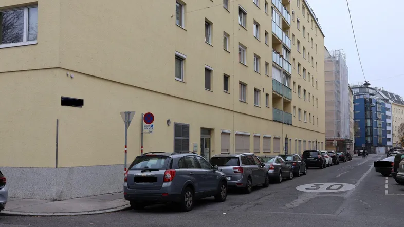 Gelbe Fassade eines Mehrfamilienhauses mit parkenden Autos auf der Straße und einem Tempo-30-Schild.