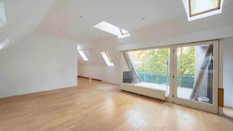 Helles Dachgeschosszimmer mit Holzboden, Dachfenstern und Zugang zu einem Balkon.