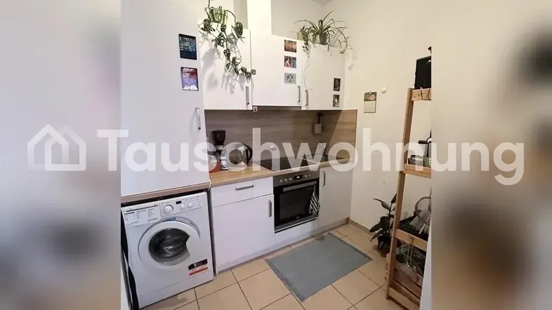 Kleine Küche mit weißen Schränken, Holzarbeitsplatte, integriertem Backofen und Waschmaschine.
