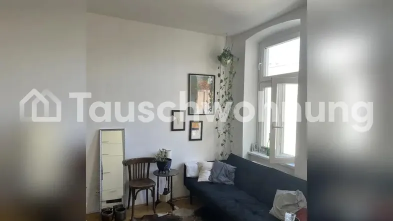 Helles Wohnzimmer mit dunklem Sofa, Holzboden und großem Fenster für natürliches Licht.
