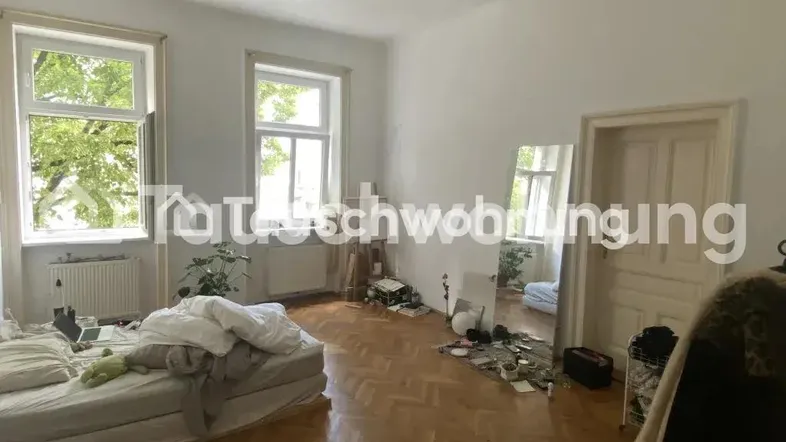Helles Schlafzimmer mit Parkettboden, hohen Decken und großen Fenstern mit Blick ins Grüne.