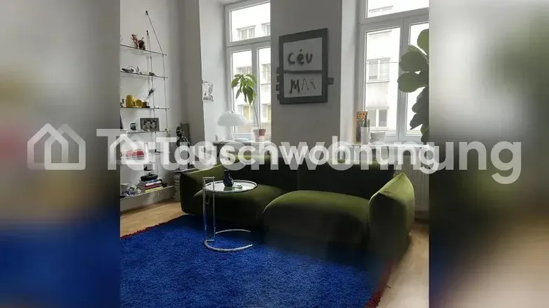 Helles Wohnzimmer mit einem olivgrünen Sofa, blauem Teppich und großen Fenstern.