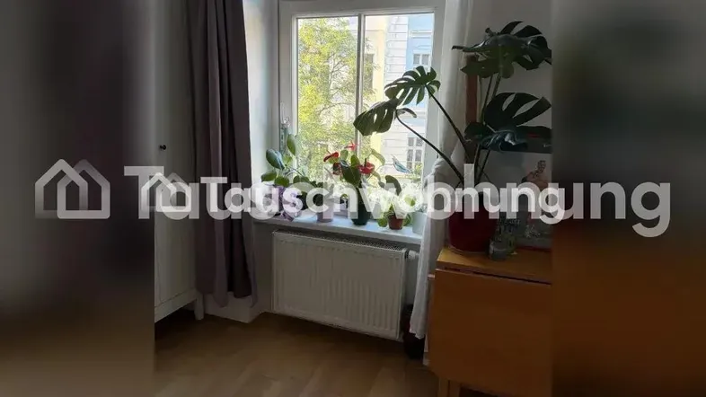 Helles Zimmer mit großem Fenster, Pflanzen auf der Fensterbank und Holzmöbeln.