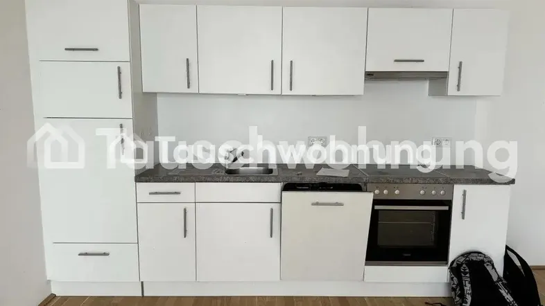 Moderne Einbauküche mit weißen Schränken, grauer Arbeitsplatte und integrierten Geräten.