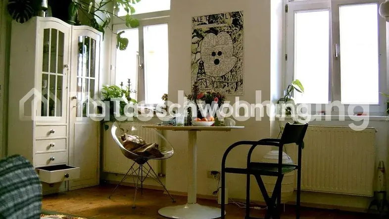 Helles Wohnzimmer mit Holzboden, vielen Pflanzen und einem kleinen Essbereich am Fenster.