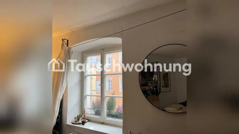 Helles Zimmer mit großem Fenster, das viel Tageslicht hereinlässt, und einem runden Spiegel an der Wand.