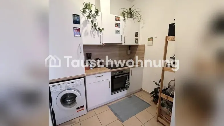 Kleine Küche mit weißen Schränken, Holzarbeitsplatte, integriertem Herd und Waschmaschine.