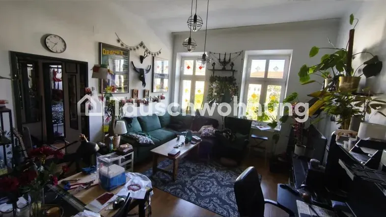 Geräumiges Wohnzimmer mit grüner Couch, Holzboden und mehreren Fenstern, die viel Licht hereinlassen.