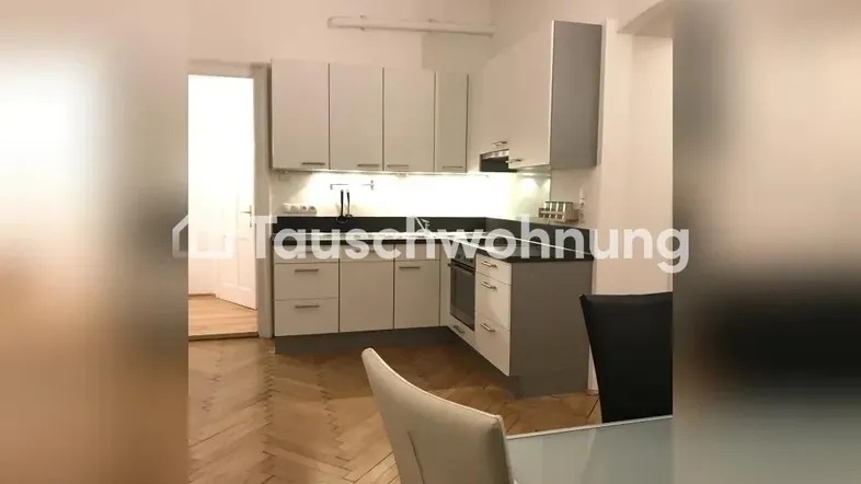 Moderne Küche mit hellen Schränken, dunkler Arbeitsplatte und Fischgrätparkettboden, offen zum Essbereich.