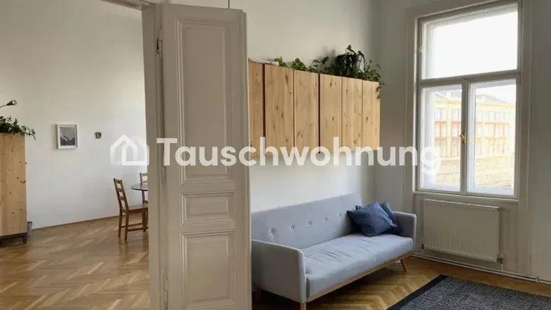 Helles Wohnzimmer mit Fischgrätparkett, einem Sofa und einem Durchgang zu einem weiteren Raum.