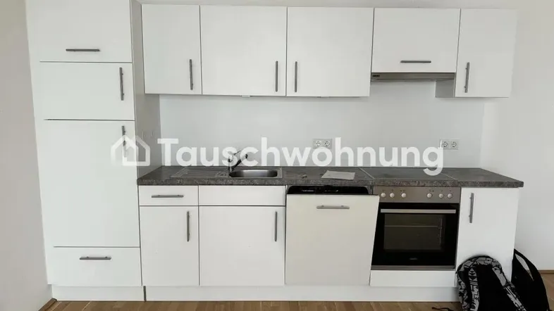 Moderne Einbauküche mit weißen Schränken, dunkler Arbeitsplatte und integrierten Geräten, auf hellem Holzfußboden.