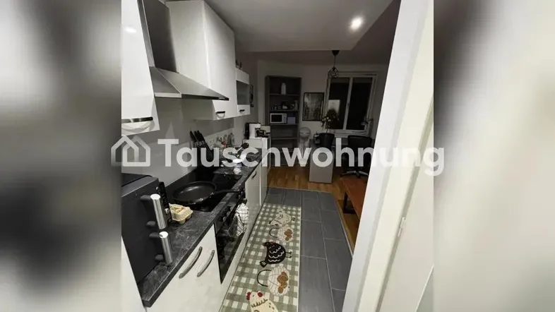 Schmale Küche mit weißen Schränken, grauen Fliesen und einem Fenster am Ende des Raumes.