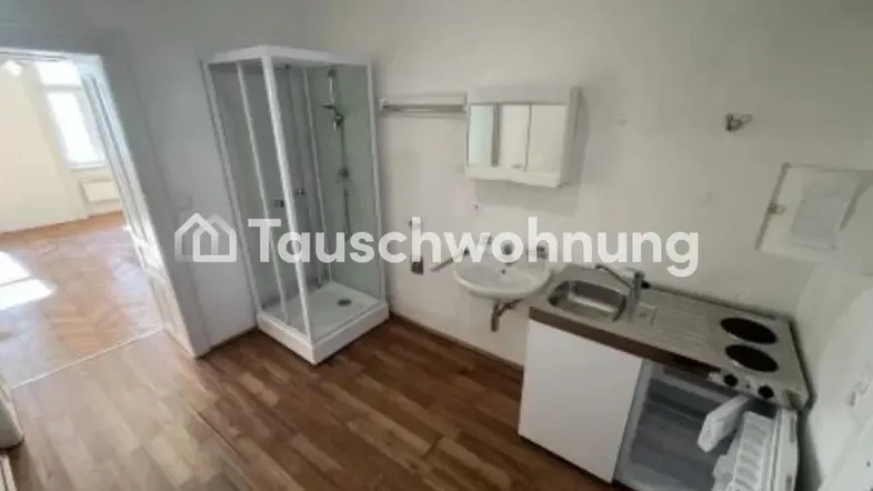 Multifunktionaler Raum mit integrierter Duschkabine, kleiner Küchenzeile und Holzboden.