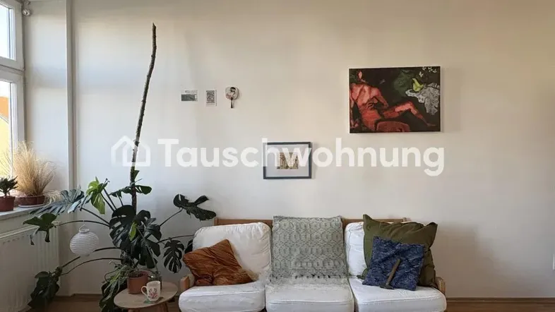 Helles Wohnzimmer mit bequemer Couch, Pflanzen und Kunstwerken an der Wand.