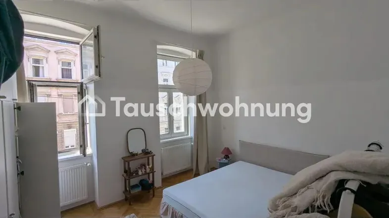 Helles Schlafzimmer mit Doppelbett, Parkettboden und zwei Fenstern mit Blick auf die Stadt.