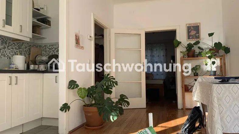 Heller offener Wohnbereich mit integrierter weißer Küche, Holzboden und Blick in ein weiteres Zimmer.