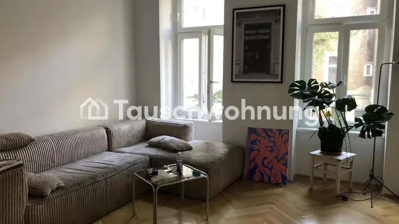 Helles Wohnzimmer mit beigem Sofa, Parkettboden und großen Fenstern, die viel Tageslicht hereinlassen.