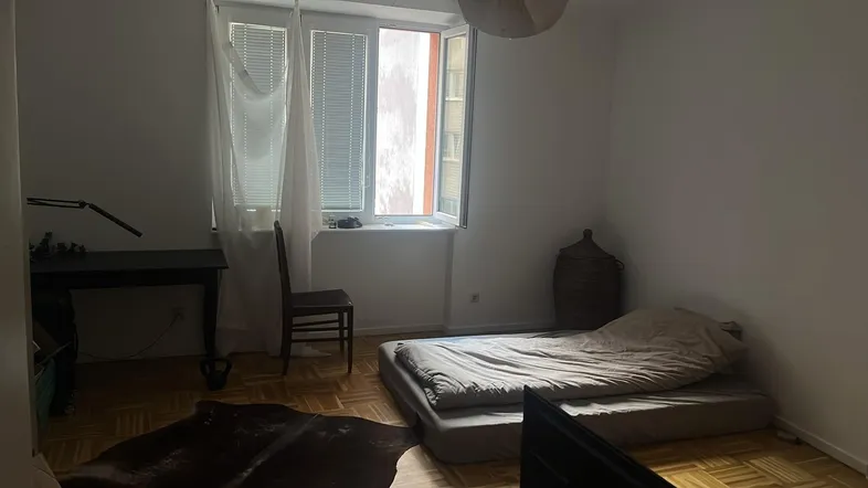 Helles Schlafzimmer mit Parkettboden, einem Bett auf dem Boden und einem Schreibtisch am Fenster.