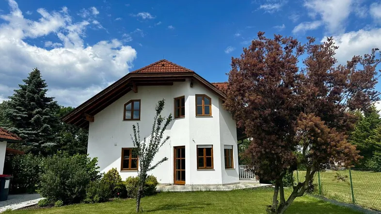 Weißes Einfamilienhaus mit Satteldach, braunen Fenstern und gepflegtem Vorgarten unter blauem Himmel.
