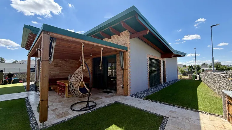 Modernes Haus mit überdachter Terrasse, Sitzbereich und gepflegtem Rasen im Außenbereich.