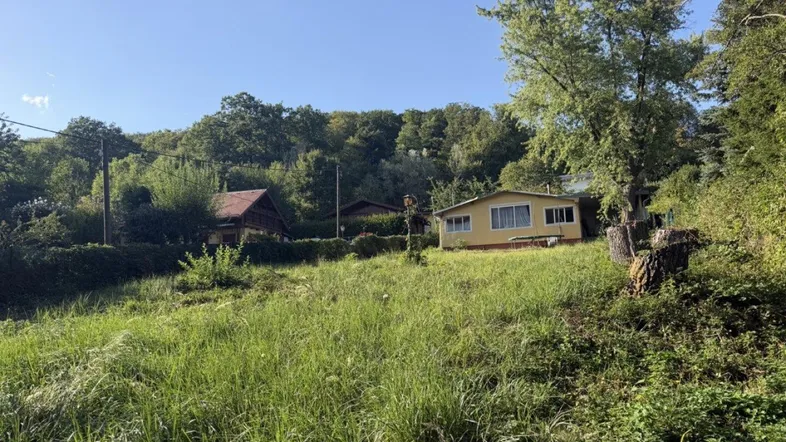 Gelbes Haus eingebettet in eine grüne Hügellandschaft mit Bäumen und Wiesen.