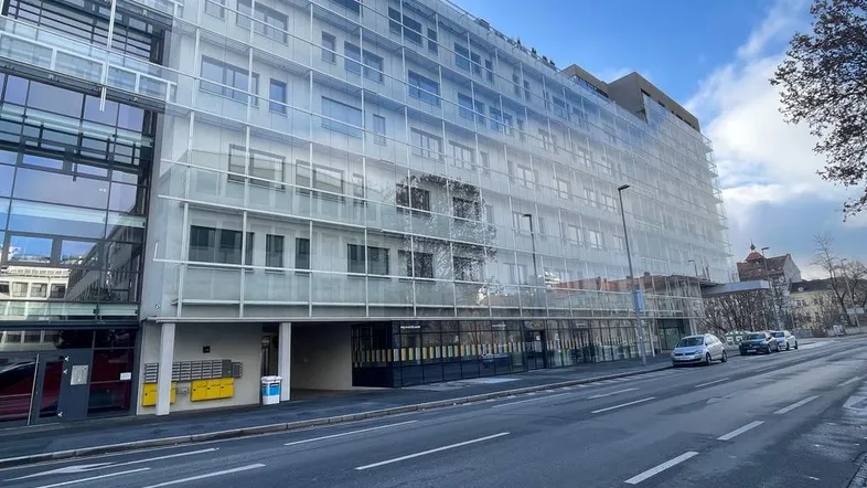 Modernes Bürogebäude mit großer Glasfassade und mehreren Etagen an einer städtischen Straße.
