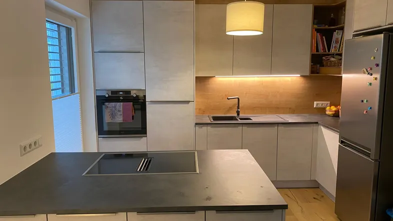 Moderne Küche mit heller Arbeitsplatte, Holzakzenten und integriertem Kochfeld auf der Kücheninsel.