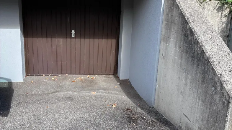 Geschlossenes Garagentor aus Holz mit Zufahrt und Betonmauer, die den Eingangsbereich begrenzt.
