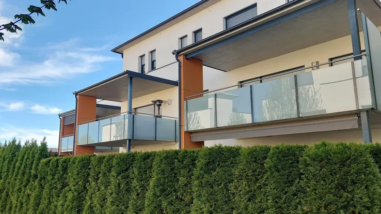 Moderne Wohngebäude mit mehreren Balkonen, Glasgeländern und ausfahrbaren Markisen.