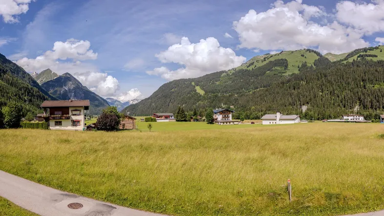 Panoramablick auf grüne Wiesen und majestätische Berge mit traditionellen Häusern in der Ferne.