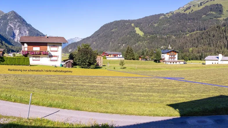Weitläufige Ansicht einer ländlichen Landschaft mit grünen Feldern, Bergen und einer schematisch markierten Grundstücksgrenze.