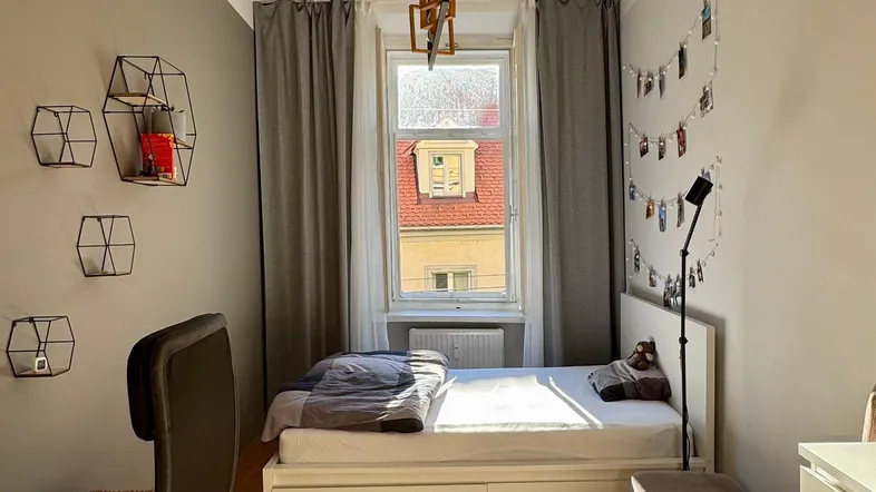 Helles Schlafzimmer mit Holzboden, Schreibtisch und einem Fenster, das Tageslicht hereinlässt.