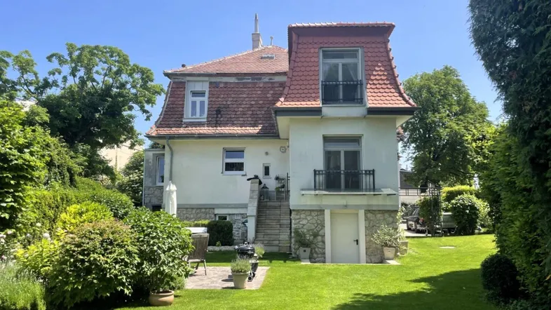 Großzügiger Gartenbereich mit Rasenfläche, Terrasse und historischer Villa im Hintergrund.
