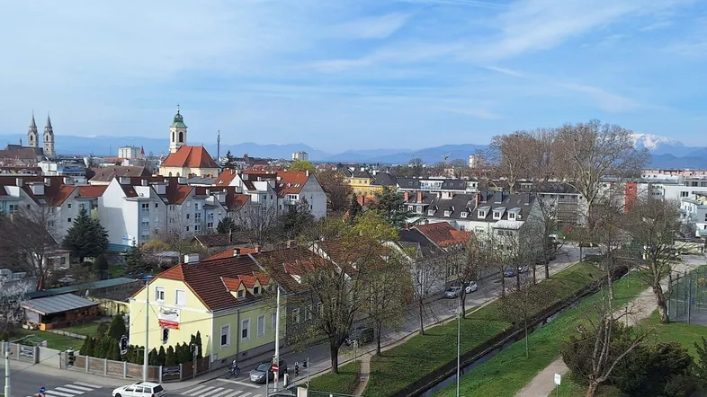 Weitläufiger Stadtblick mit historischen Gebäuden und Bergen im Hintergrund.