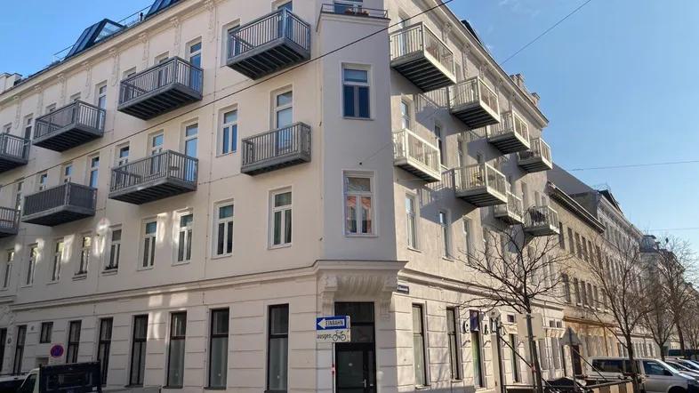 Eckgebäude mit mehreren Balkonen und moderner Architektur unter blauem Himmel.