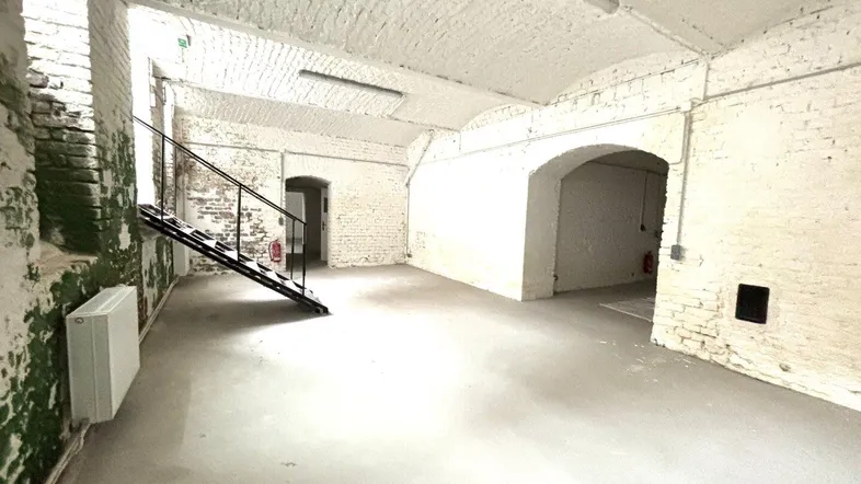 Geräumiger Kellerraum mit weiß gestrichenen Ziegelwänden, Betonboden, gewölbter Decke und einer Metalltreppe.