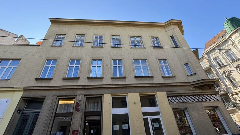 Die Fassade des Gebäudes zeigt mehrere Stockwerke mit vielen Fenstern und Geschäften im Erdgeschoss.