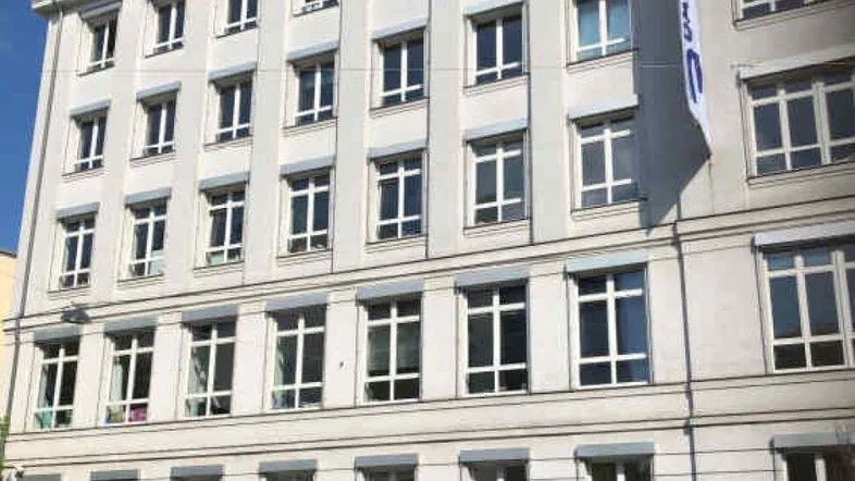 Die moderne Fassade des Bürogebäudes mit zahlreichen Fenstern und Jalousien unter blauem Himmel.