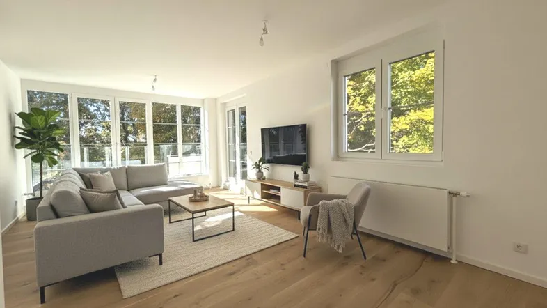 Helles Wohnzimmer mit großen Fenstern, Holzboden und moderner Einrichtung, bietet viel Tageslicht.