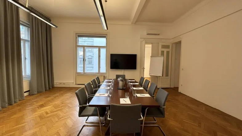 Großer Konferenzraum mit elegantem Holztisch, modernen Pendelleuchten und Fischgrätparkettboden.