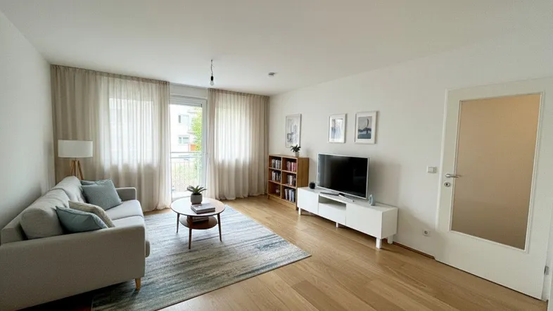 Helles Wohnzimmer mit Parkettboden, bequemer Couch und Zugang zum Balkon.