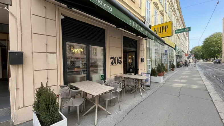 Außenansicht eines Cafés mit Markise und Tischen auf dem Bürgersteig in einer städtischen Umgebung.