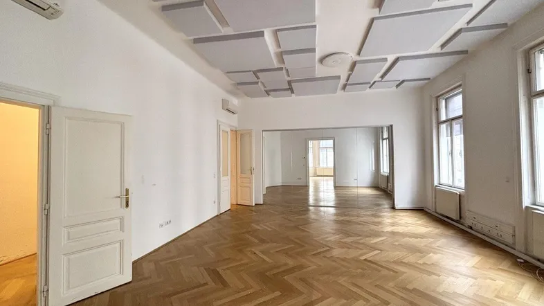 Geräumiger Raum mit Fischgrätparkett, Schalldämmplatten an der Decke und großen Fenstern.