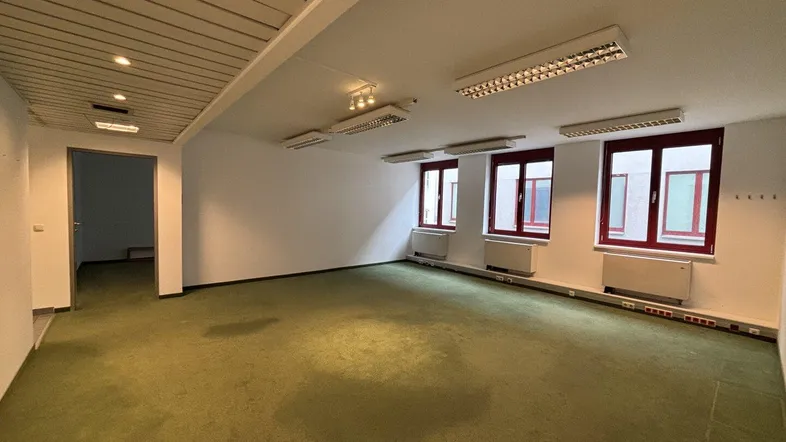 Geräumiges Büro mit grünem Teppichboden, weißen Wänden und mehreren Fenstern, ideal für Arbeitsbereiche.