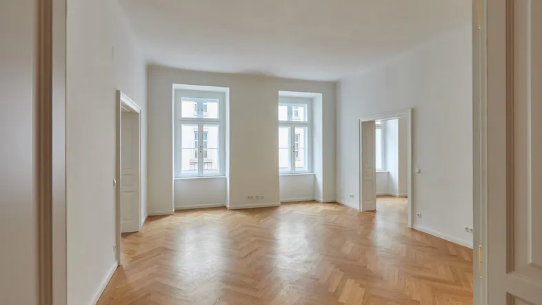 Helles, leeres Zimmer mit Fischgrätparkett und hohen Fenstern, bereit zur individuellen Gestaltung.