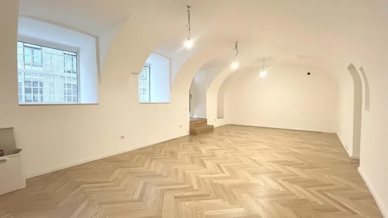 Geräumiger, leerer Raum mit elegantem Fischgrätparkett, weißen Wänden und charakteristischen Gewölbedecken.