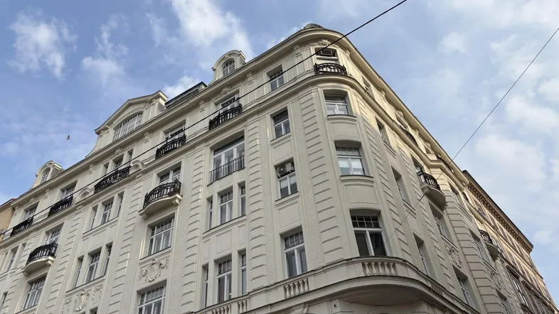 Elegante Fassade eines Altbaus mit klassischen Balkonen und Verzierungen unter blauem Himmel.